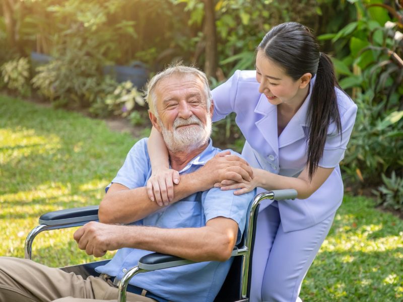 happy-nurse-holding-elderly-man-hand-wheelchair-garden-nursing-home